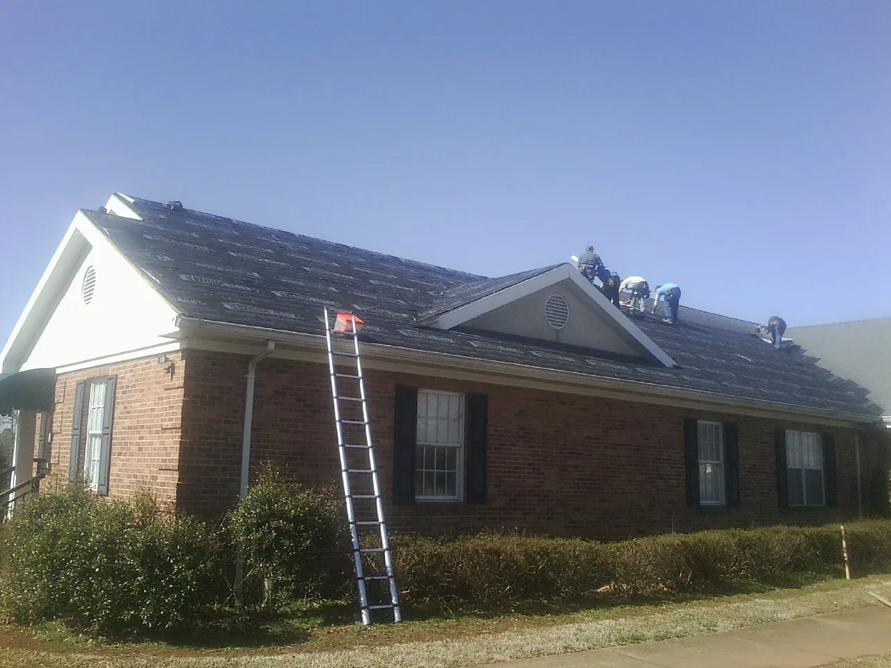 Crew tearing shingles off a brick ranch roof with a ladder set — Metal Roof Repair work by our crew in Trout Creek