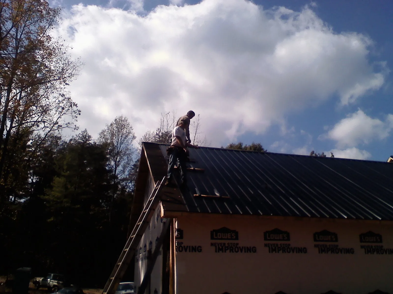Roofer fastening dark metal panels high against a cloudy sky, from a Roof Inspection job in Trout Creek